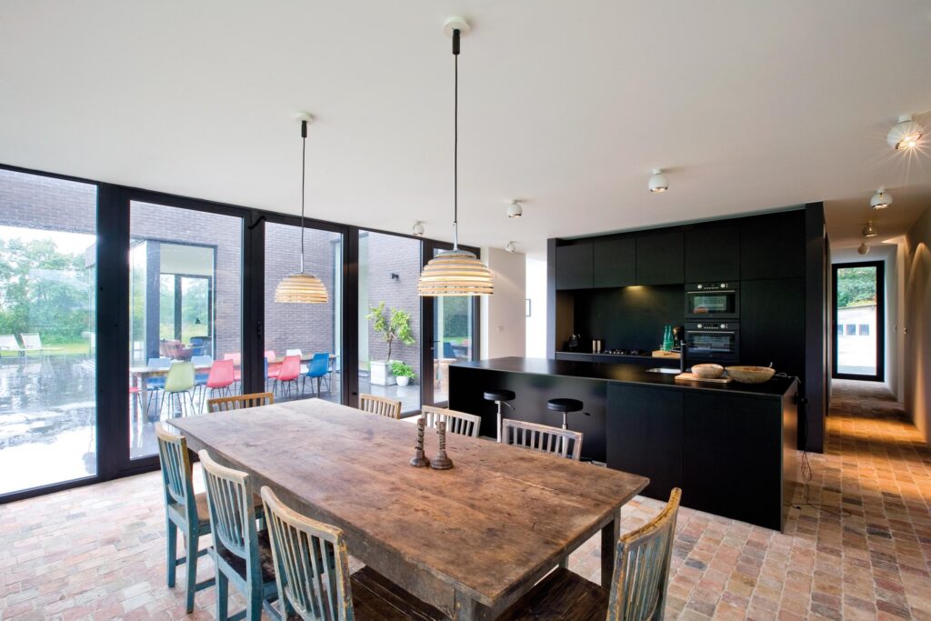 Open keuken en eethoek met houten tafel en grote ramen &mdash; woning De Bruycker, Aartselaar